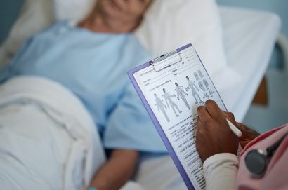 Medical professional checking patient's health chart while patient rests in hospital bed under care showing detailed examination and attentive care