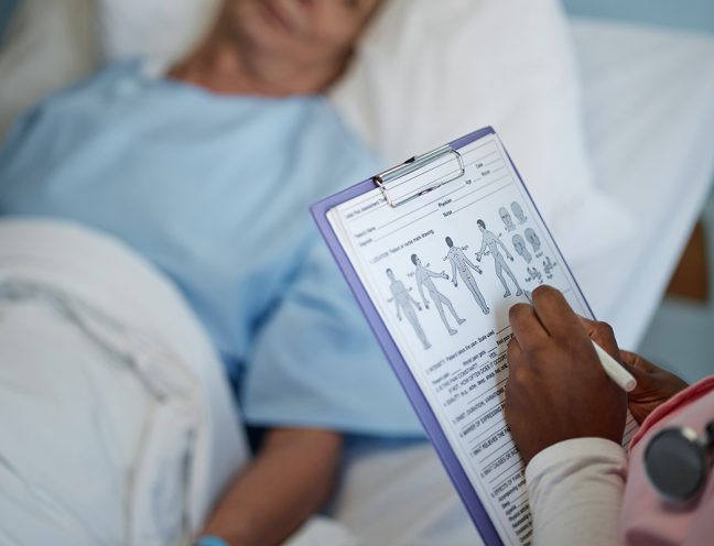 Medical Professional Reviewing Patient's Health Chart Medical professional checking patient's health chart while patient rests in hospital bed under care showing detailed examination and attentive care